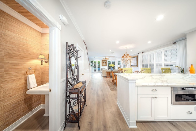 kitchen with white cabinetry, oven, ornamental molding, light stone countertops, and light wood-type flooring