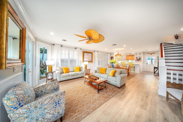 living room with ceiling fan with notable chandelier, light hardwood / wood-style flooring, ornamental molding, and plenty of natural light