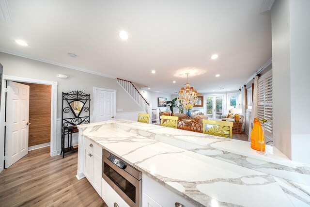 kitchen with stainless steel microwave, white cabinetry, ornamental molding, light stone counters, and light hardwood / wood-style flooring