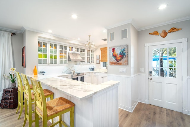 kitchen featuring crown molding, a kitchen breakfast bar, kitchen peninsula, light hardwood / wood-style floors, and white cabinets