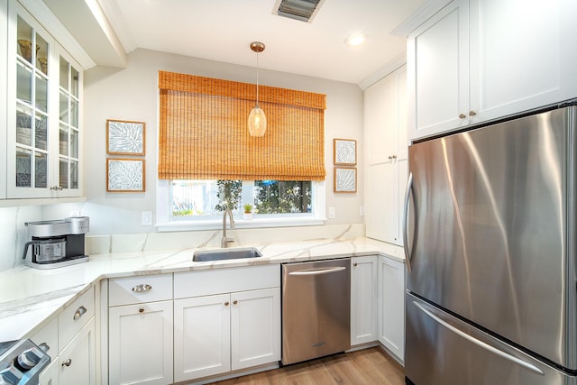 kitchen with appliances with stainless steel finishes, decorative light fixtures, white cabinetry, sink, and light stone counters