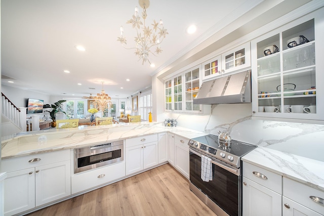 kitchen with appliances with stainless steel finishes, white cabinetry, hanging light fixtures, a notable chandelier, and wall chimney exhaust hood