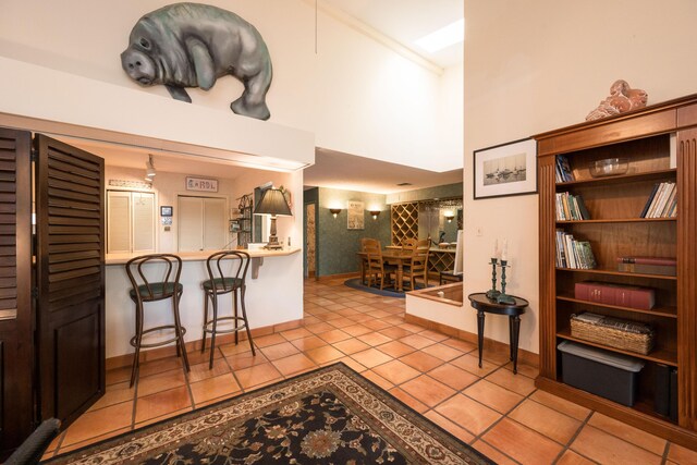 kitchen with a kitchen bar, a high ceiling, ornamental molding, light tile patterned floors, and kitchen peninsula