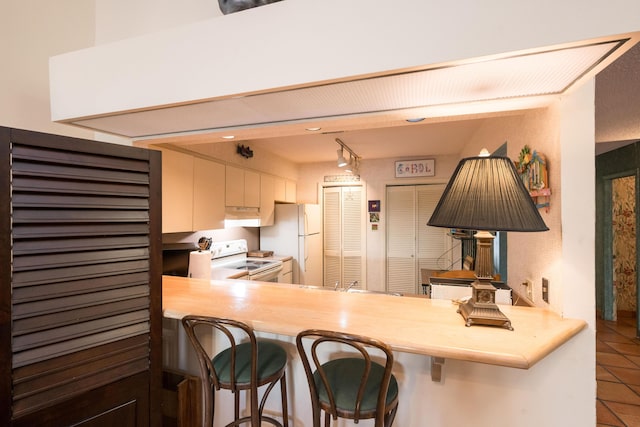 kitchen featuring white appliances, tile patterned floors, kitchen peninsula, and a kitchen bar