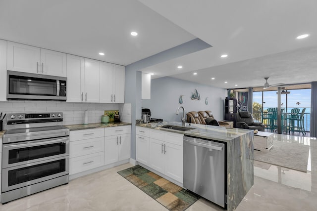 kitchen with stainless steel appliances, backsplash, open floor plan, a sink, and a peninsula