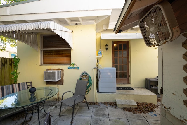 view of exterior entry featuring a patio, stucco siding, a wall mounted AC, outdoor dining space, and washer / dryer