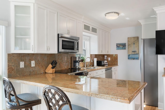 kitchen with a breakfast bar area, stainless steel appliances, white cabinetry, and kitchen peninsula