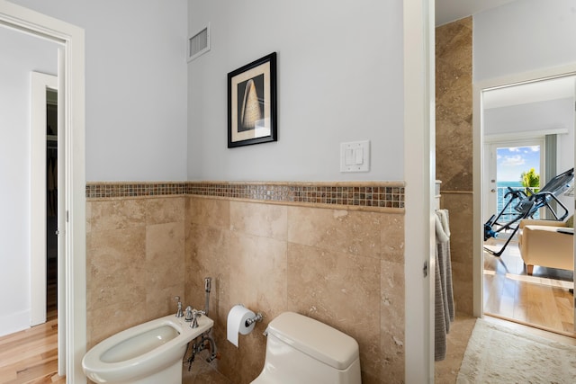 bathroom with a bidet, tile walls, and toilet