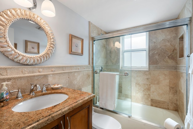 full bathroom featuring toilet, tile walls, enclosed tub / shower combo, and vanity