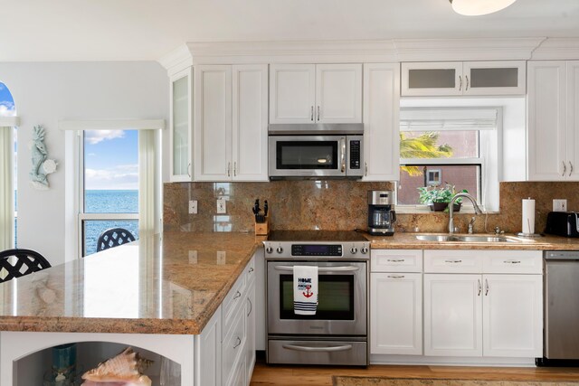 kitchen with appliances with stainless steel finishes, a water view, sink, and white cabinets