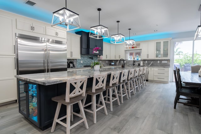 kitchen featuring visible vents, decorative backsplash, a breakfast bar area, light stone counters, and white cabinetry