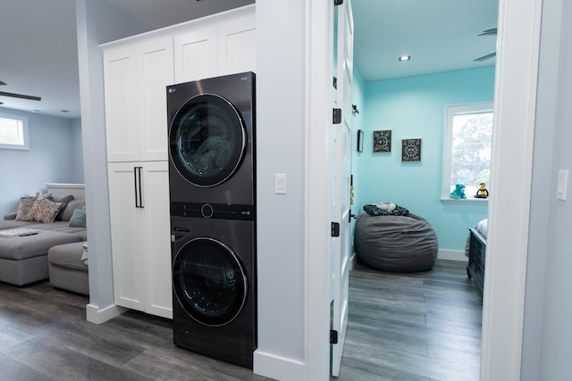 laundry room featuring stacked washer and dryer, a wealth of natural light, dark wood-style flooring, and cabinet space