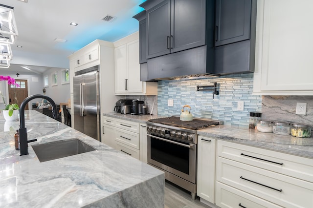 kitchen with premium appliances, a sink, visible vents, decorative backsplash, and light stone countertops