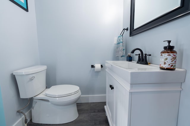 half bathroom with baseboards, vanity, toilet, and wood finished floors