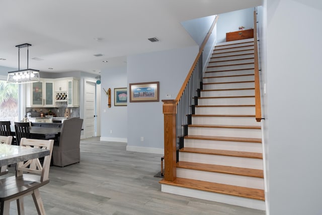 staircase featuring an inviting chandelier, visible vents, baseboards, and wood finished floors