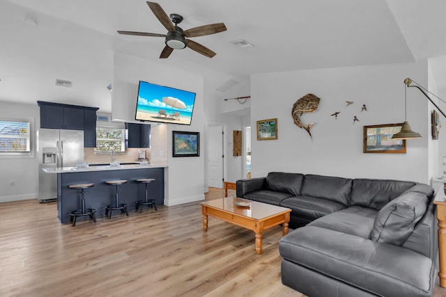 living room with ceiling fan, a wealth of natural light, vaulted ceiling, and light wood-type flooring