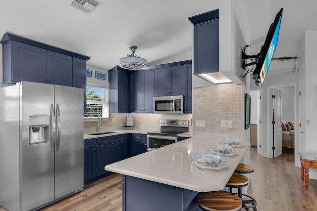 kitchen with blue cabinetry, a breakfast bar, sink, appliances with stainless steel finishes, and decorative backsplash