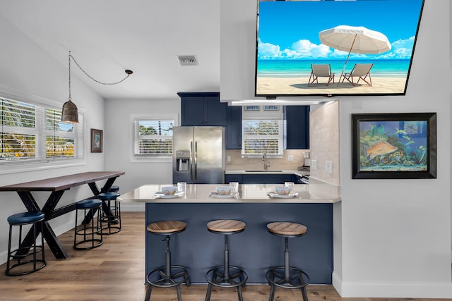 kitchen with sink, stainless steel fridge, a breakfast bar area, light hardwood / wood-style floors, and decorative backsplash