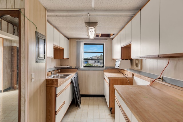 kitchen with white cabinetry, sink, wooden walls, and hanging light fixtures