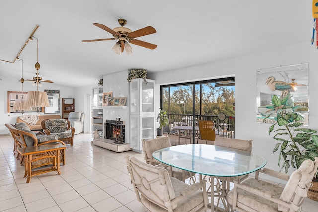 dining space with ceiling fan, a tiled fireplace, and light tile patterned floors