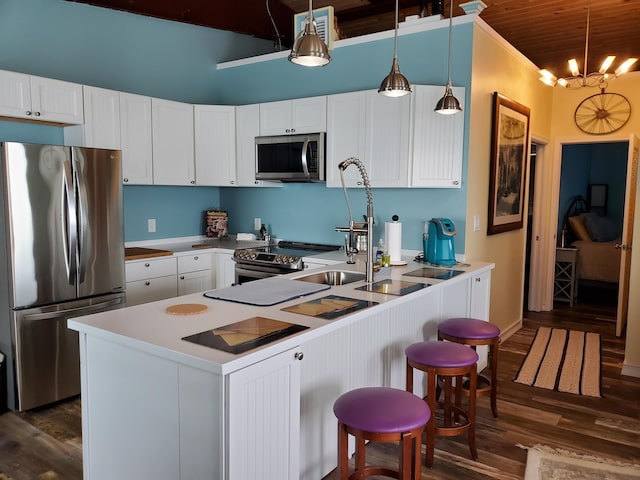 kitchen with dark wood-type flooring, a breakfast bar area, appliances with stainless steel finishes, white cabinets, and decorative light fixtures