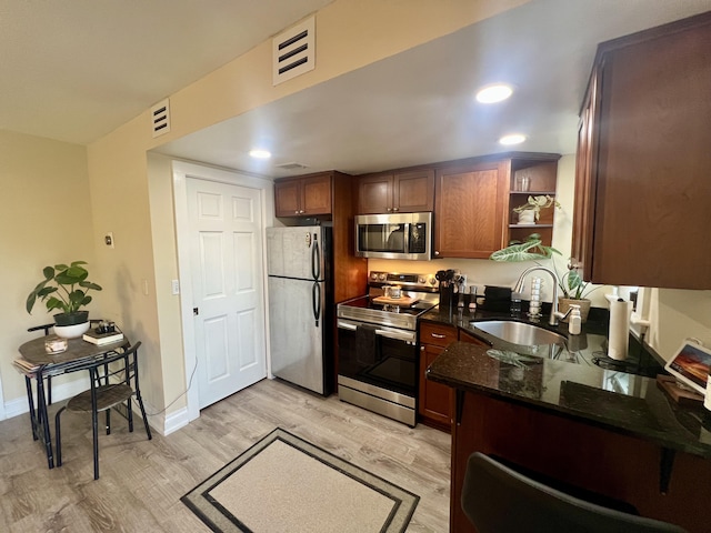 kitchen with stainless steel appliances, sink, dark stone countertops, and light hardwood / wood-style floors