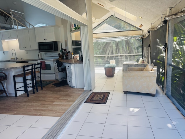 kitchen featuring electric stove, sink, high vaulted ceiling, white cabinets, and light tile patterned flooring