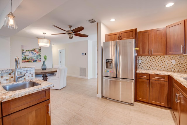 kitchen featuring stainless steel refrigerator with ice dispenser, sink, pendant lighting, and light stone counters