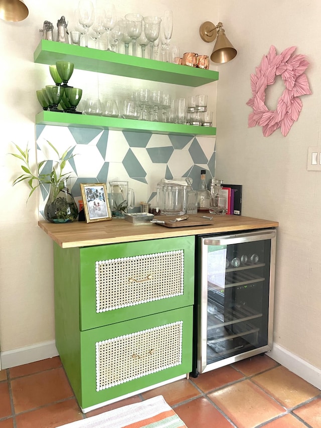 bar with beverage cooler, green cabinets, and dark tile patterned floors