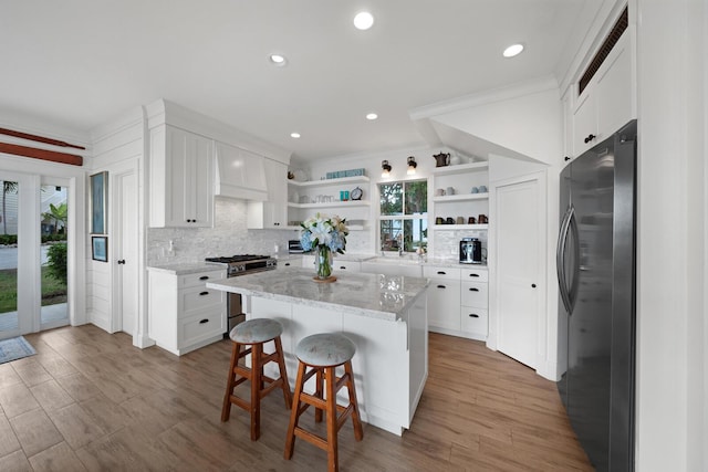 kitchen featuring black refrigerator, a breakfast bar, white cabinetry, a center island, and stainless steel range with gas stovetop