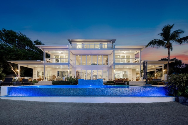 back house at dusk with a patio area, outdoor lounge area, pool water feature, and a balcony