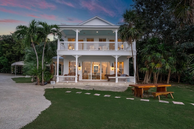 back house at dusk with a balcony, a carport, covered porch, and a lawn