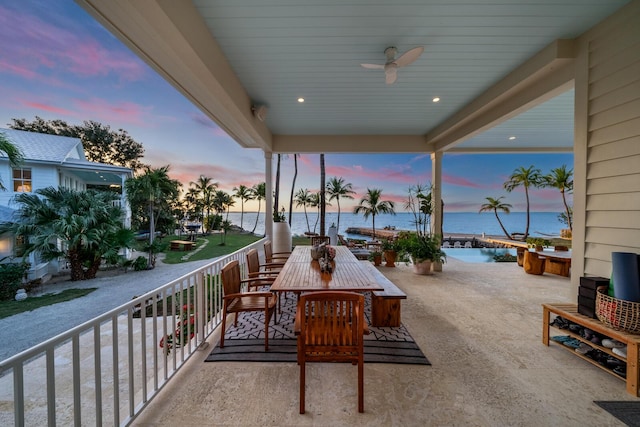 patio terrace at dusk featuring a water view and ceiling fan