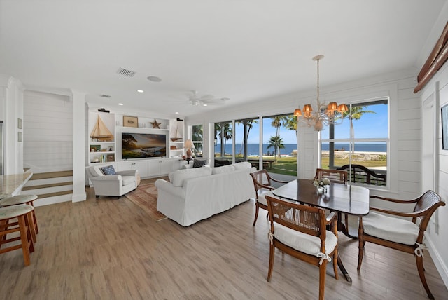 dining space featuring ceiling fan with notable chandelier, light hardwood / wood-style floors, and built in shelves