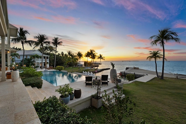 pool at dusk featuring a water view, a yard, and a patio