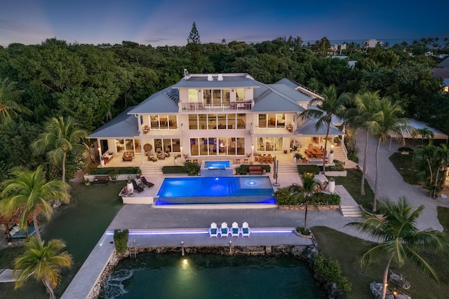 back house at dusk featuring a swimming pool with hot tub, an outdoor living space, a patio, and a balcony