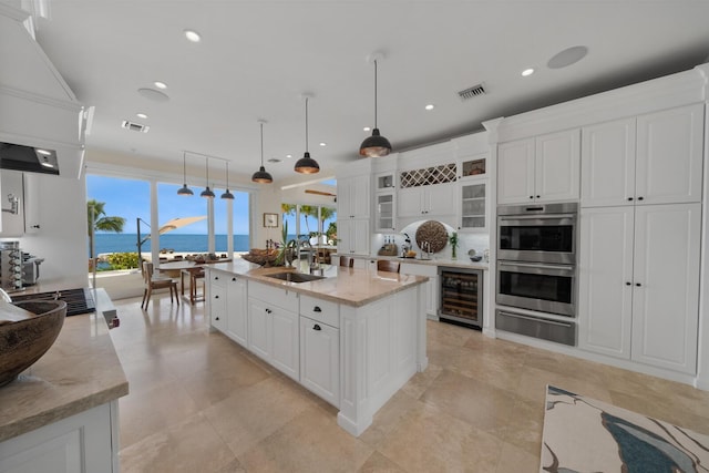 kitchen with a water view, white cabinetry, beverage cooler, and pendant lighting