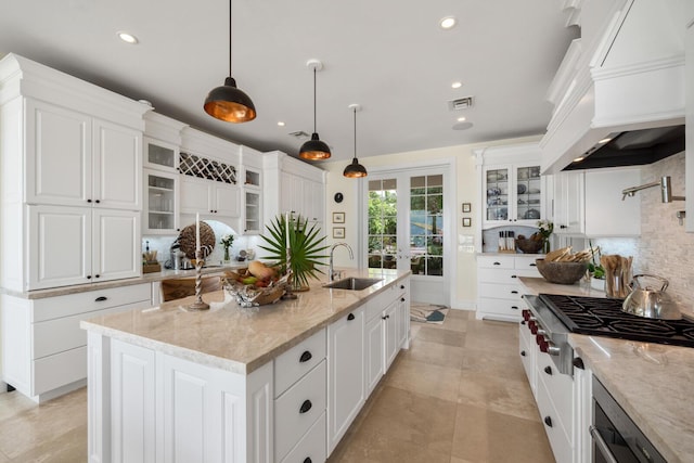 kitchen with premium range hood, stainless steel gas cooktop, sink, an island with sink, and pendant lighting