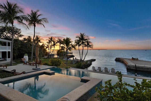 pool at dusk with a water view, a hot tub, and a patio