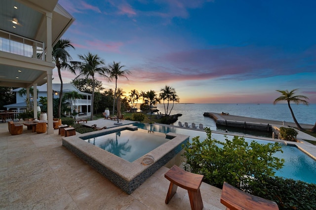 pool at dusk with a patio area, an in ground hot tub, and a water view