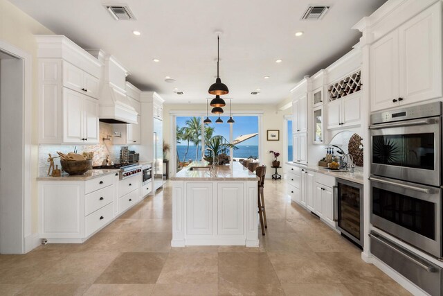 kitchen featuring hanging light fixtures, appliances with stainless steel finishes, white cabinets, and beverage cooler