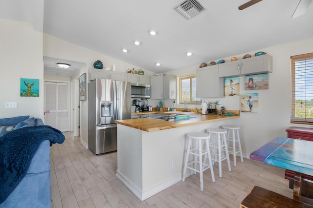 kitchen featuring lofted ceiling, butcher block countertops, appliances with stainless steel finishes, a kitchen breakfast bar, and kitchen peninsula