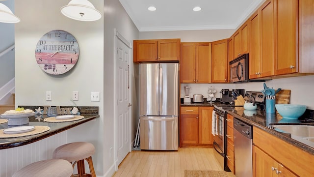 kitchen featuring crown molding, appliances with stainless steel finishes, dark stone countertops, light hardwood / wood-style floors, and a kitchen bar