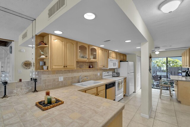 kitchen featuring sink, tasteful backsplash, light tile patterned floors, light brown cabinets, and white appliances