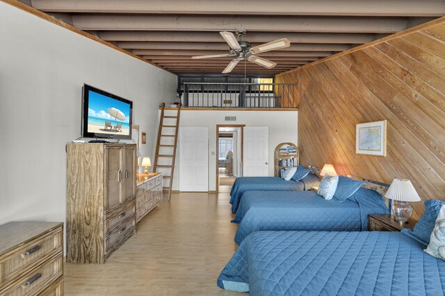 bedroom with a towering ceiling, light hardwood / wood-style floors, beamed ceiling, and wood walls