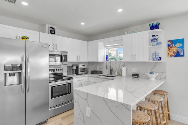 kitchen featuring white cabinetry, light stone countertops, appliances with stainless steel finishes, and a sink