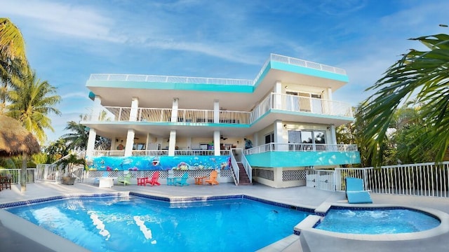 back of property with a swimming pool with hot tub, a balcony, and a patio area