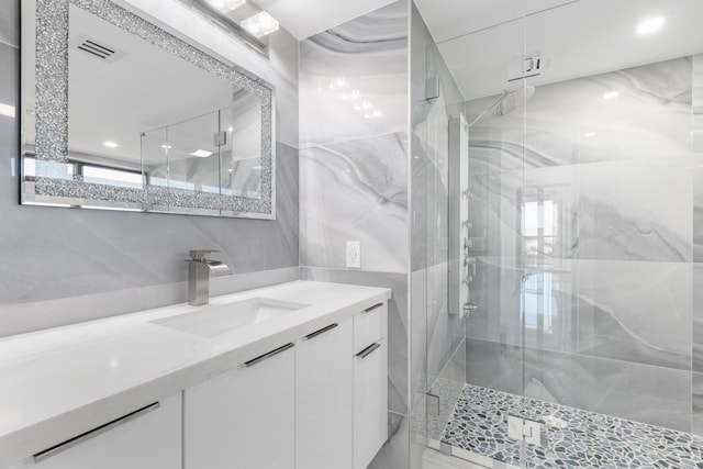 bathroom with a marble finish shower, tile walls, vanity, and visible vents