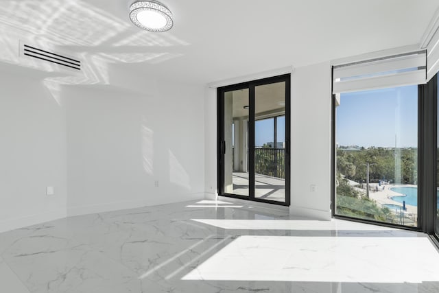 empty room featuring floor to ceiling windows, visible vents, marble finish floor, and baseboards