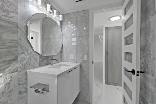 bathroom with marble finish floor, vanity, and tile walls